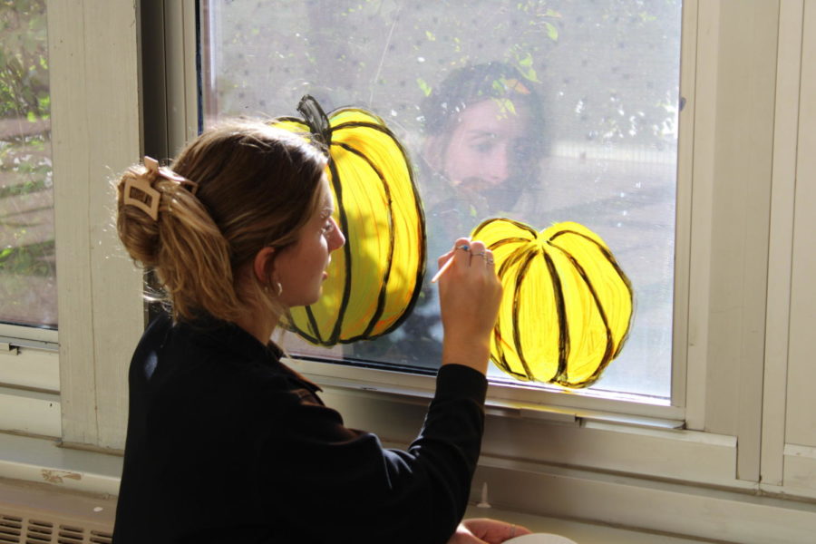 Member, Grace O’Keefe, is painting pumpkins along the breezeway windows leading to the English hallway.